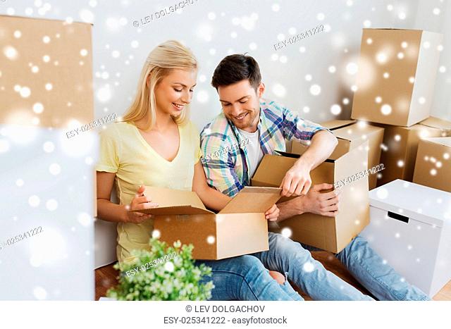 home, people and real estate concept - smiling couple with many cardboard boxes moving to new place over snow