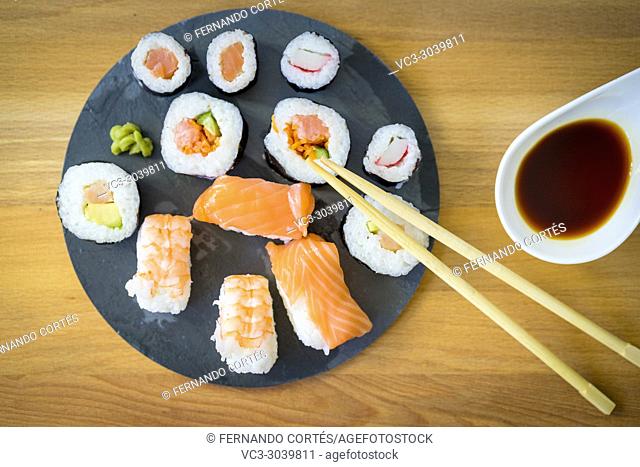 Sushi on a wooden table on black slate plate with soy sauce and chopsticks