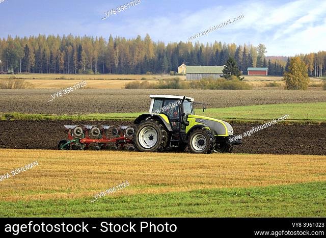 Farmer plows field with green Valtra tractor and plough on a sunny autumn morning in South of Finland. Jokioinen, Finland. October 2, 2020
