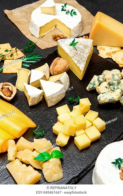 various types of cheese - brie, camembert, roquefort and cheddar on dark concrete background