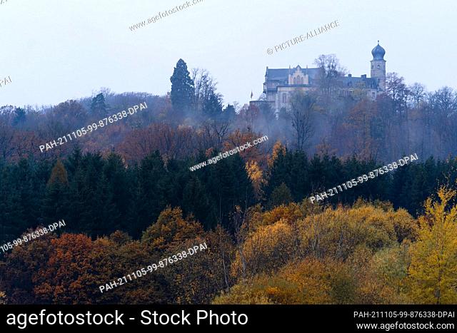 dpatop - 05 November 2021, Bavaria, Coburg: Morning mist rises between the autumnally coloured trees near the Veste Coburg