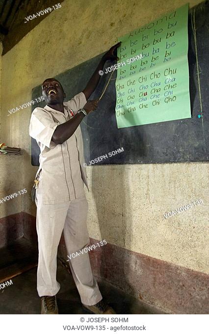 Teacher of English syllables to children in blue uniforms at school behind desk near Tsavo National Park, Kenya, Africa
