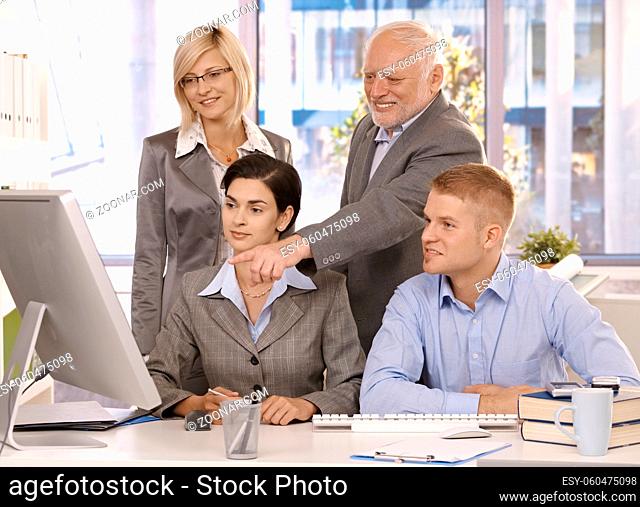Experienced senior executive working with businessteam, pointing at computer screen, smiling