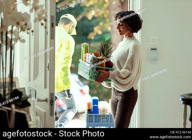 Woman receiving grocery delivery from courier at front door