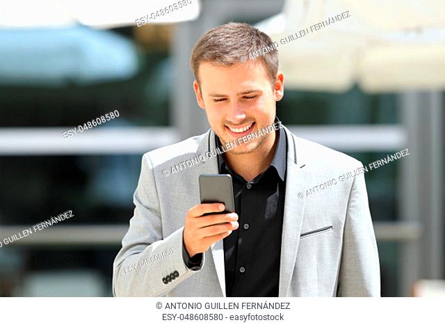 Front view portrait of a young businessman walking towards camera and texting on phone
