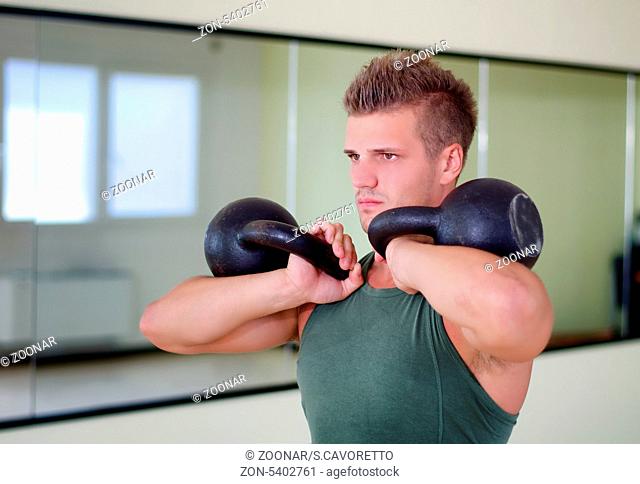 Attractive young athletic man exercising in gym, working out using kettlebells