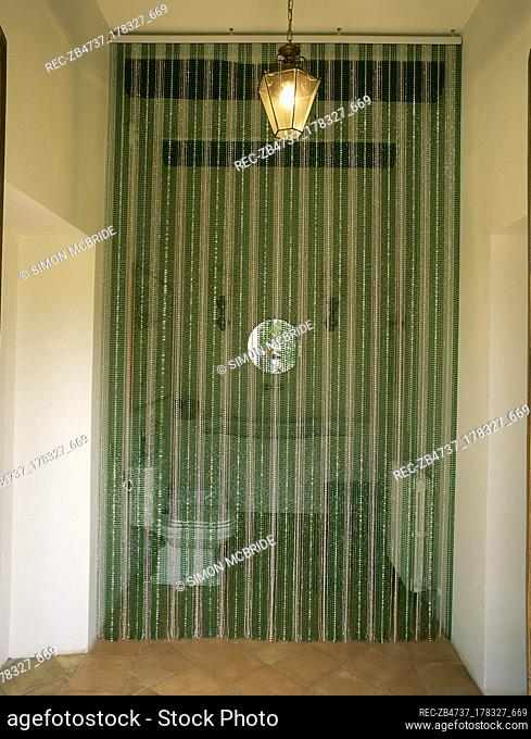 Beaded curtain over the doorway to a small bathroom with wooden beams and a lit lantern