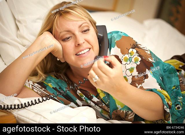 Beautiful blonde woman laying on her bed using the telephone