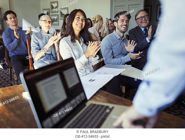 Smiling business people clapping for businessman leading conference presentation at laptop
