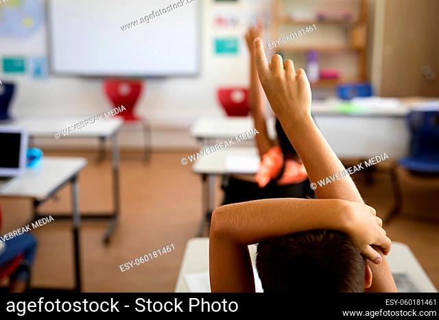 Rear view of boy raising his hand for participation in the class at elementary school