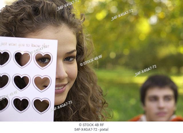 Teenage girl holding a romantic postcard in front of her face, close-up, selective focus