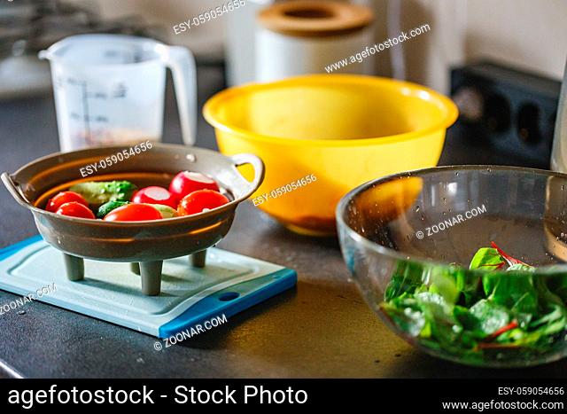 Washed vegetables in a colander on the kitchen table for making salad - radishes, cucumbers, tomatoes, herbs