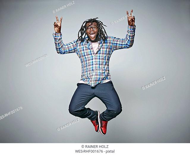 Screaming man with dreadlocks jumping in the air while showing victory signs