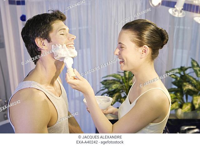 Young woman applying shaving cream to young man