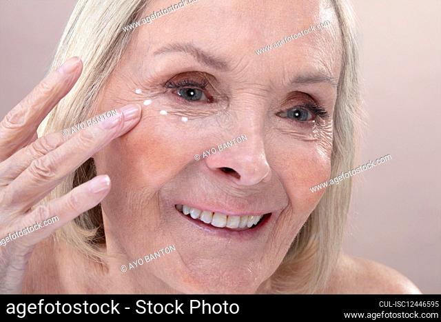 Studio shot of senior woman applying eye cream