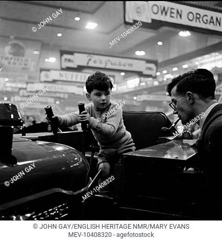 A young boy on a Fordson tractor, with a man at the side smoking a pipe, at the Royal Smithfield Show at Earls Court