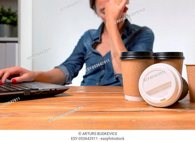 Tired businesswoman in the office with many to go coffee cups on the table