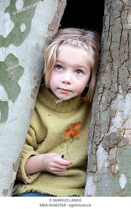 6-year-old girl with pensive view sit in a concave tree