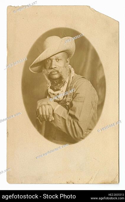 Photographic postcard portrait of a man wearing a hat and overalls, early 20th century. Creator: Unknown