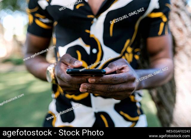 Hands of young man using phone in public park