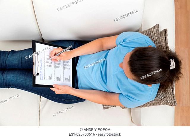 High Angle View Of Woman Sitting On Sofa While Filling Survey Form