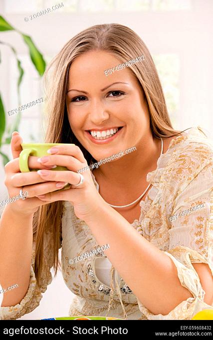 Beautiful young woman holding cup of tea in hand, smiling