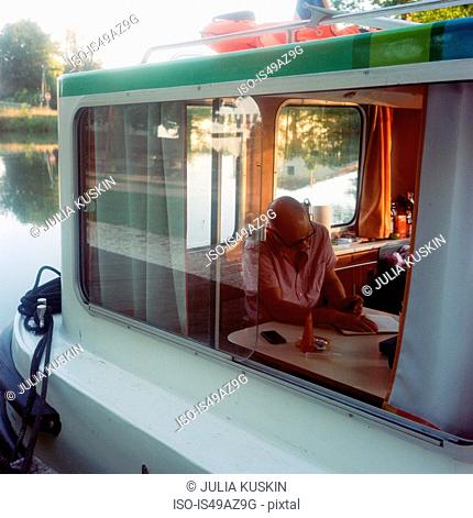 Mature man sitting inside barge, on water