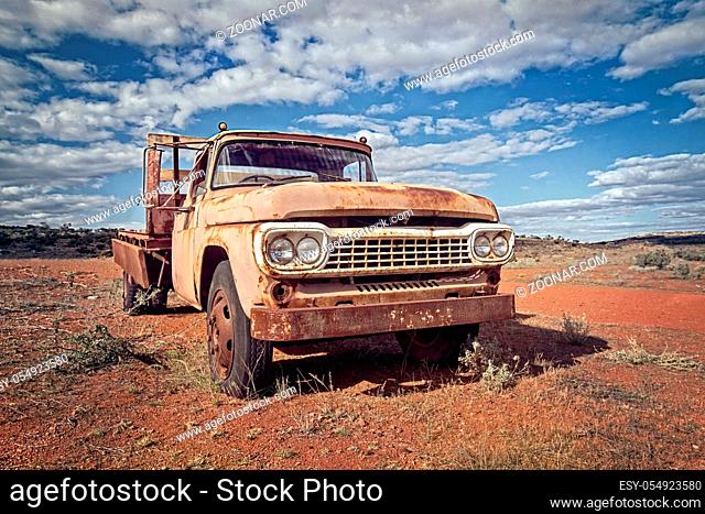 Australia – Outback desert with an old vintage abandoned car near the track under cloudy sky