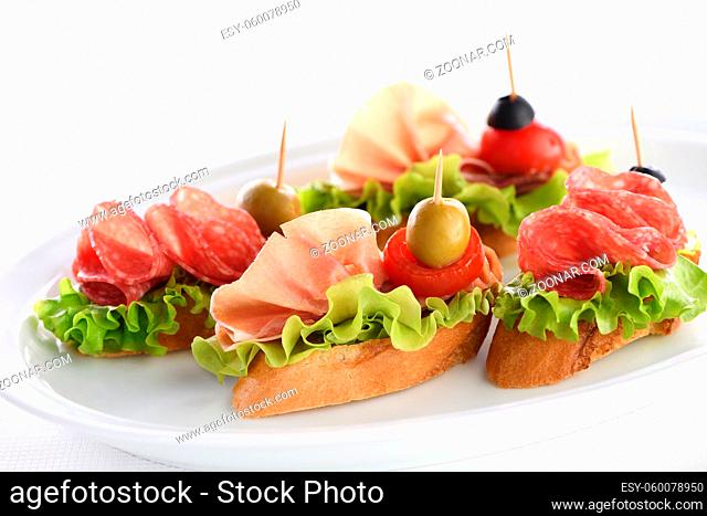 Tender baguette canapes with Leaf lettuce, salami or Parma ham, tomatoes, mozzarella and olive. Delicacy assorted platter for at the party