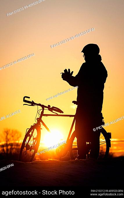 12 February 2021, Bremen: A cyclist puts on his gloves at sunrise at Lake Werder. Photo: Sina Schuldt/dpa. - Bremen/Bremen/Germany