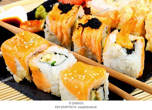 Arrangement of Various Maki Sushi with Smoked Salmon, Eel and Tempura Crab on Stone Plate closeup on Straw Mat background