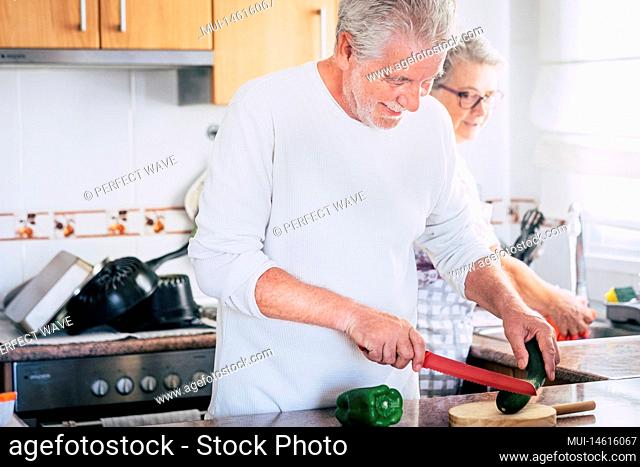 Old couple laughing together - adult man is kooking and smilng - senior woman is washing and cleaning - people having fun and enjoying at home in the kitchen