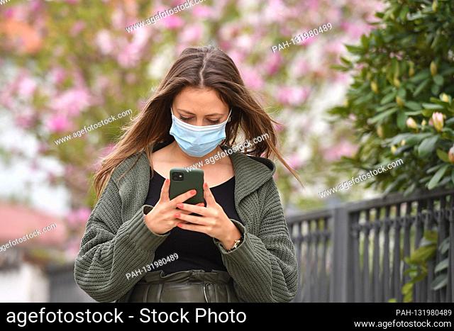 Topic image Corona: A young woman with protective mask, face mask, community mask looks at her smartphone on April 24th, 2020. | usage worldwide