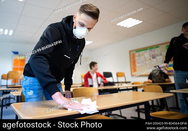 23 April 2020, North Rhine-Westphalia, Ìbach-Palenberg: A student wearing a protective mask disinfects his desk after the basic computer science course of the...