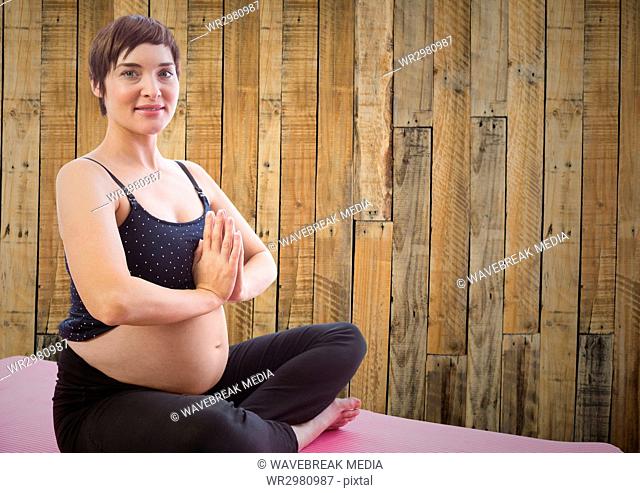 Pregnant woman meditating against wood panel