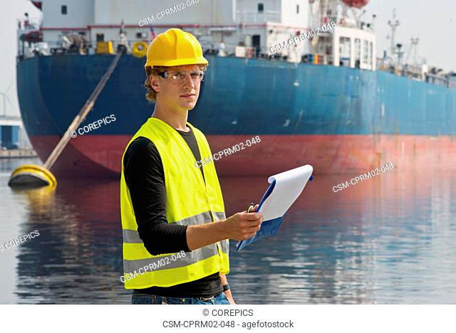 Docker looking up from his notes, standing in front of a large container ship