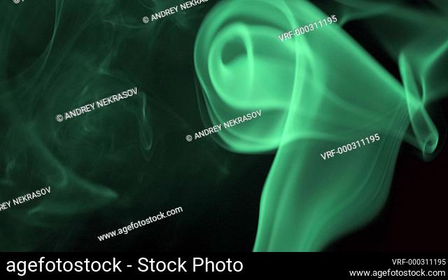 Thin trickle of bright neon green smoke slowly rising graceful twists up on black background. Colored smoke blowing from bottom to top. Closeup
