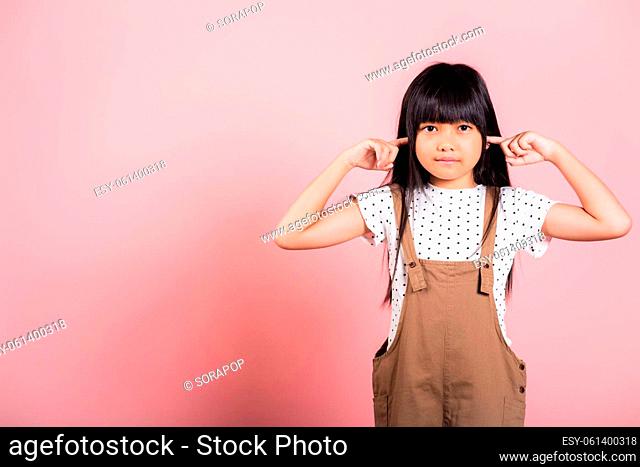 Asian little kid 10 years old Close her ears with fingers and eyes at studio shot isolated on pink background, child girl does not want to listen