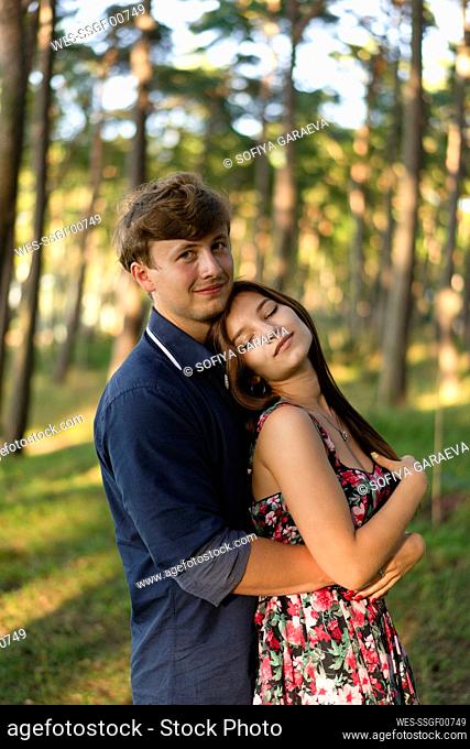 Woman with eyes closed leaning head on boyfriend's shoulder in forest