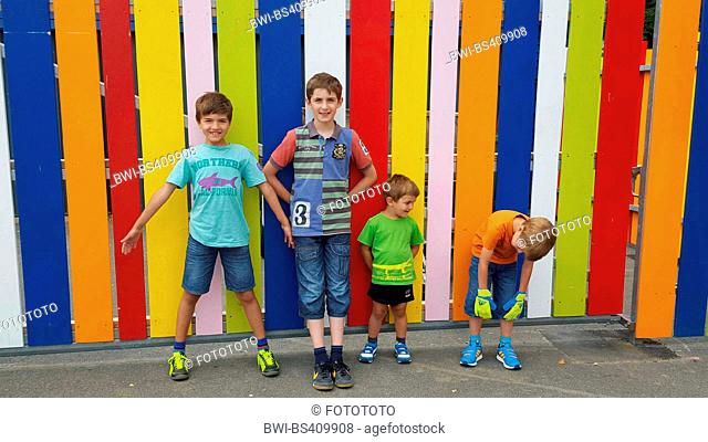 four brothers standing in front of a colorful batten fence