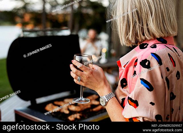 Woman holding wine glass and barbecuing meat