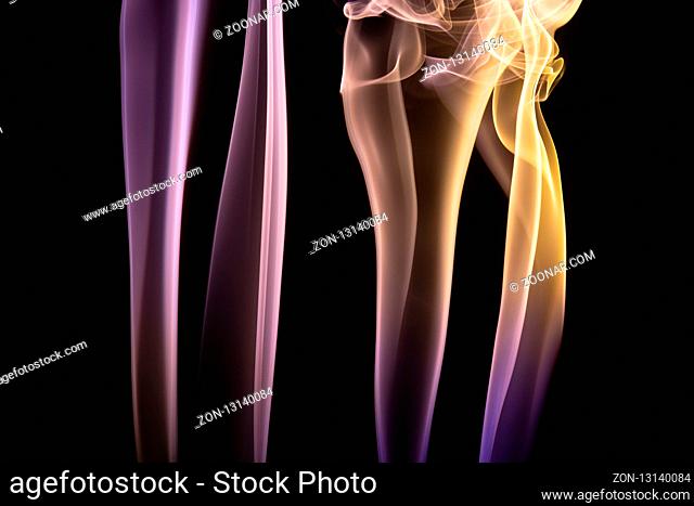 Colorful purple and yellow smoke of incence sticks isolated at black background