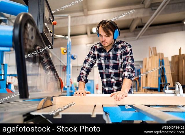 Industrial worker cutting wood in machine while standing at industry
