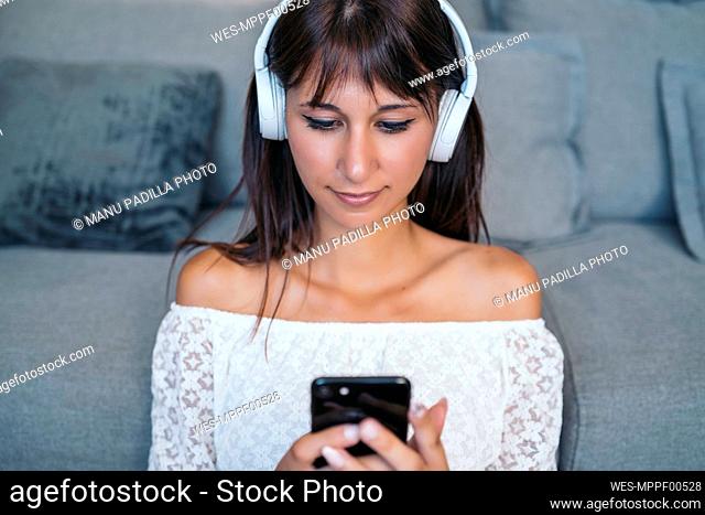Portrait of young woman listening to music with headphones in the living room at home