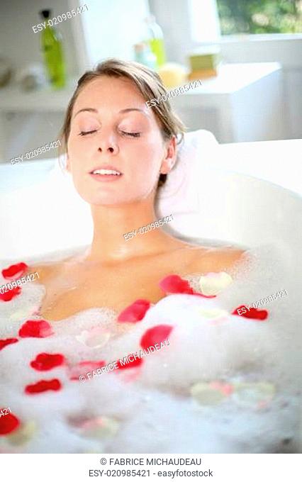 Beautiful woman relaxing in bath with rose petals