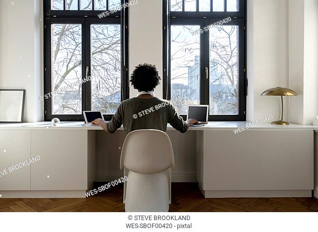 Man working in front of panorama window at home with laptop and tablet