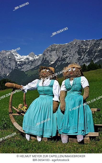 Two straw dolls or figures in dirndl dresses sitting on a sledge with long horn-shaped runners on a meadow, Ramsau bei Berchtesgaden