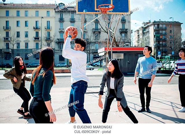 Young female and male adult friends playing basketball on city court