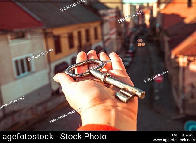 The big old key lies on a woman's hand. Woman demonstrates a steel key on a background of the city. The concept of key from town