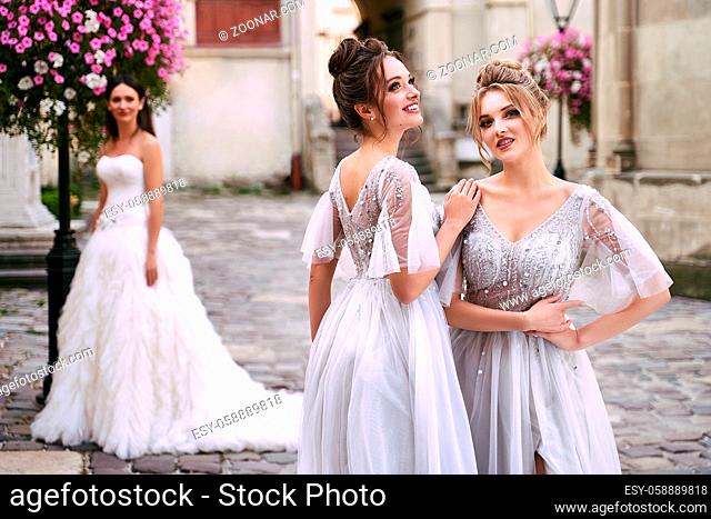 Beautiful bride and bridesmaids in gorgeous light silver dresses in old beautiful European city on a wedding day in summer